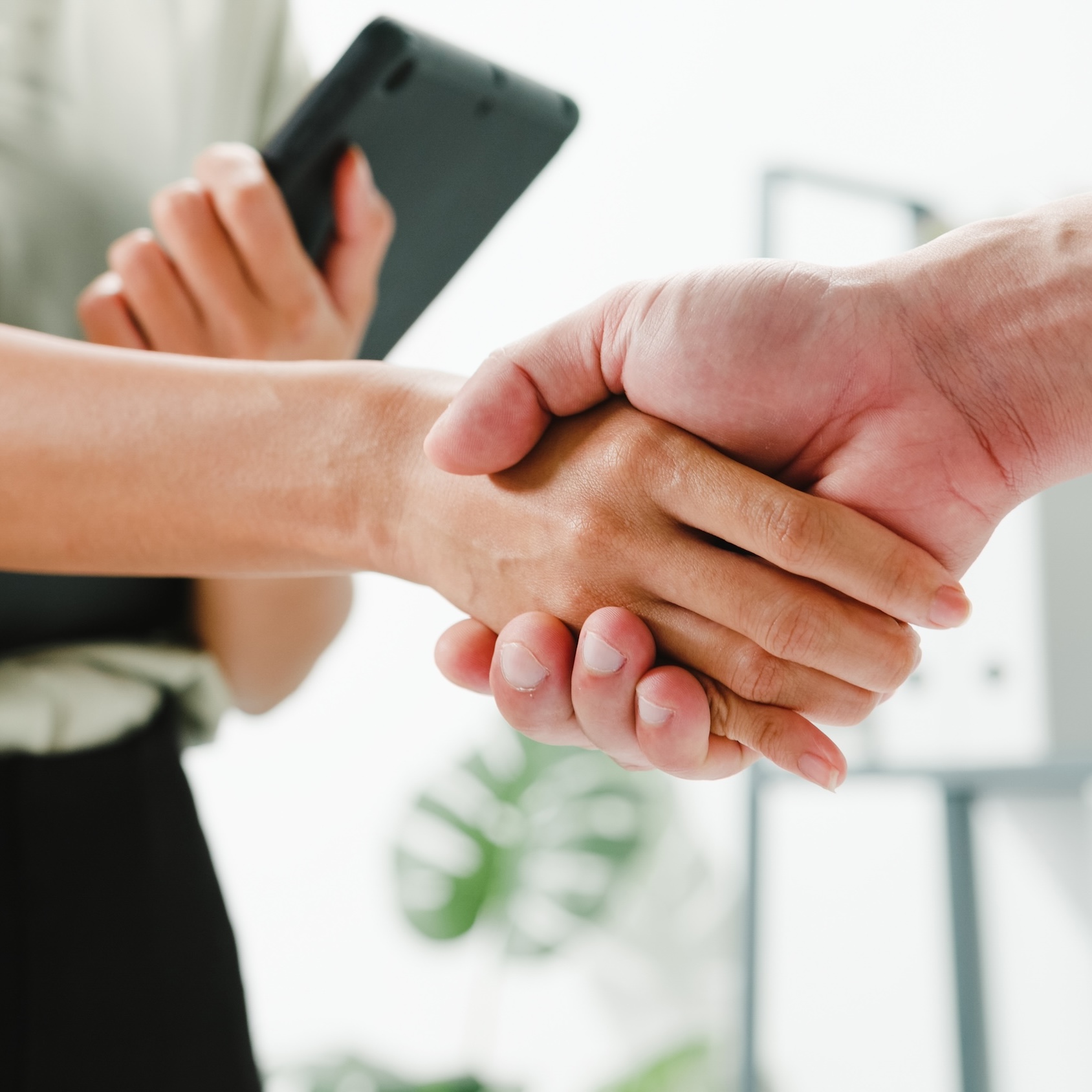 Multiracial group of young creative people in smart casual wear discussing business shaking hands together and smiling while standing in modern office. Partner cooperation, coworker teamwork concept.
